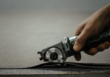 A hand holds a circular cutting tool against a piece of fabric, poised to make a precise cut along its edge.