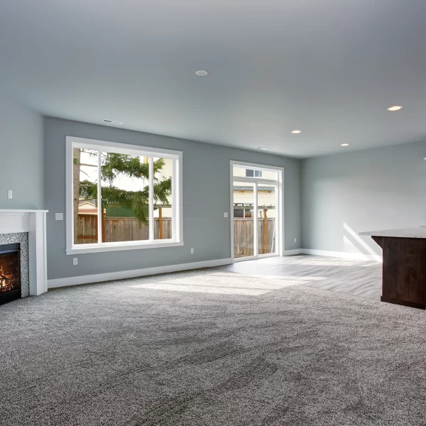 Open concept living room featuring plush grey carpeting, a white mantel fireplace, and an adjacent kitchen area with dark wood island.